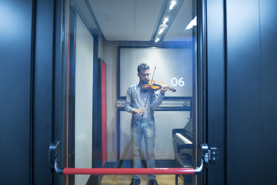 A male student practising on the violin, in a solo practise pod, at the H漫画.